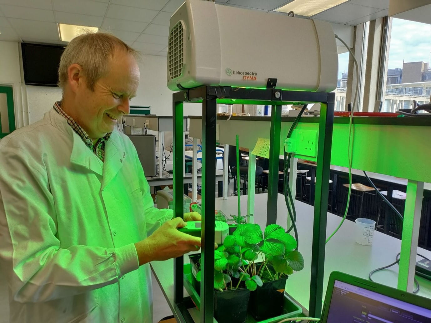 smiling technician holding a piece of equipment over a plant